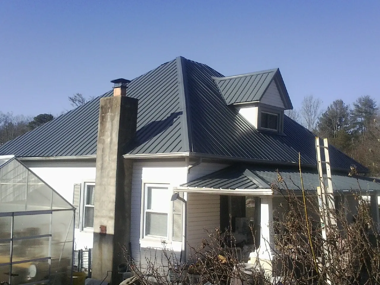 Dark blue standing seam metal roof on a white farmhouse with dormer — Slate & Tile Roof Repair by Roofing Brothers in Elkwood