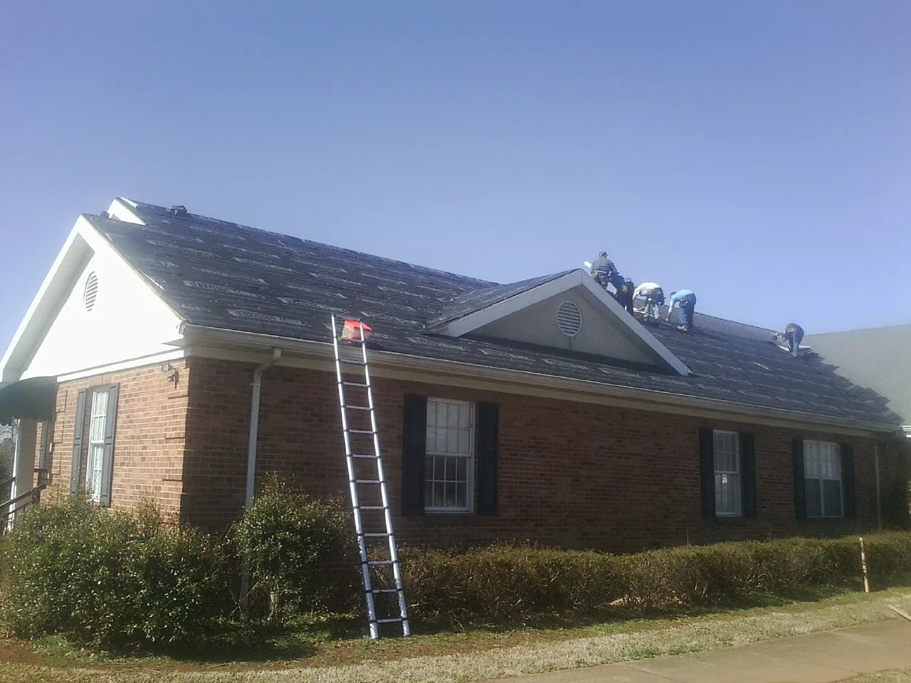 Crew tearing shingles off a brick ranch roof with a ladder set — Emergency Roof Repair work by our crew in Elkwood