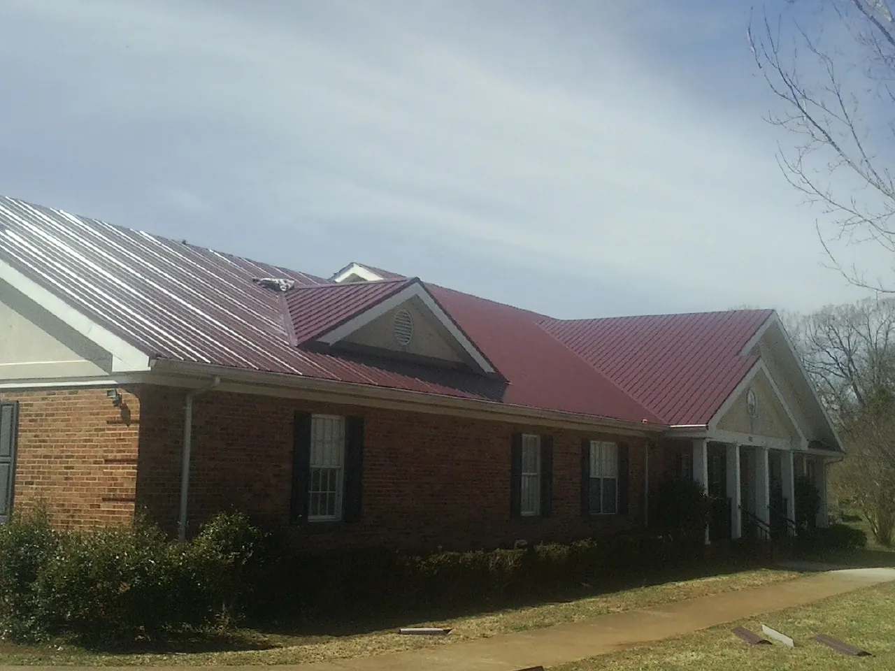 Red metal roof with gabled entries on a long brick building, from a Hail Damage Roof Repair job in Elkwood