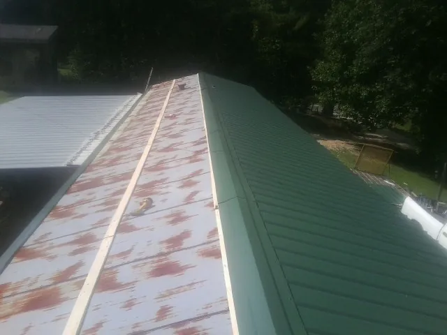 Old rusted panels beside newly installed green metal roofing — Wind Damage Roof Repair by Roofing Brothers in Elkwood