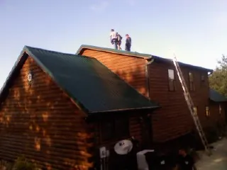 Crew on the ridge of a green metal roof on a two story log home in Elkwood