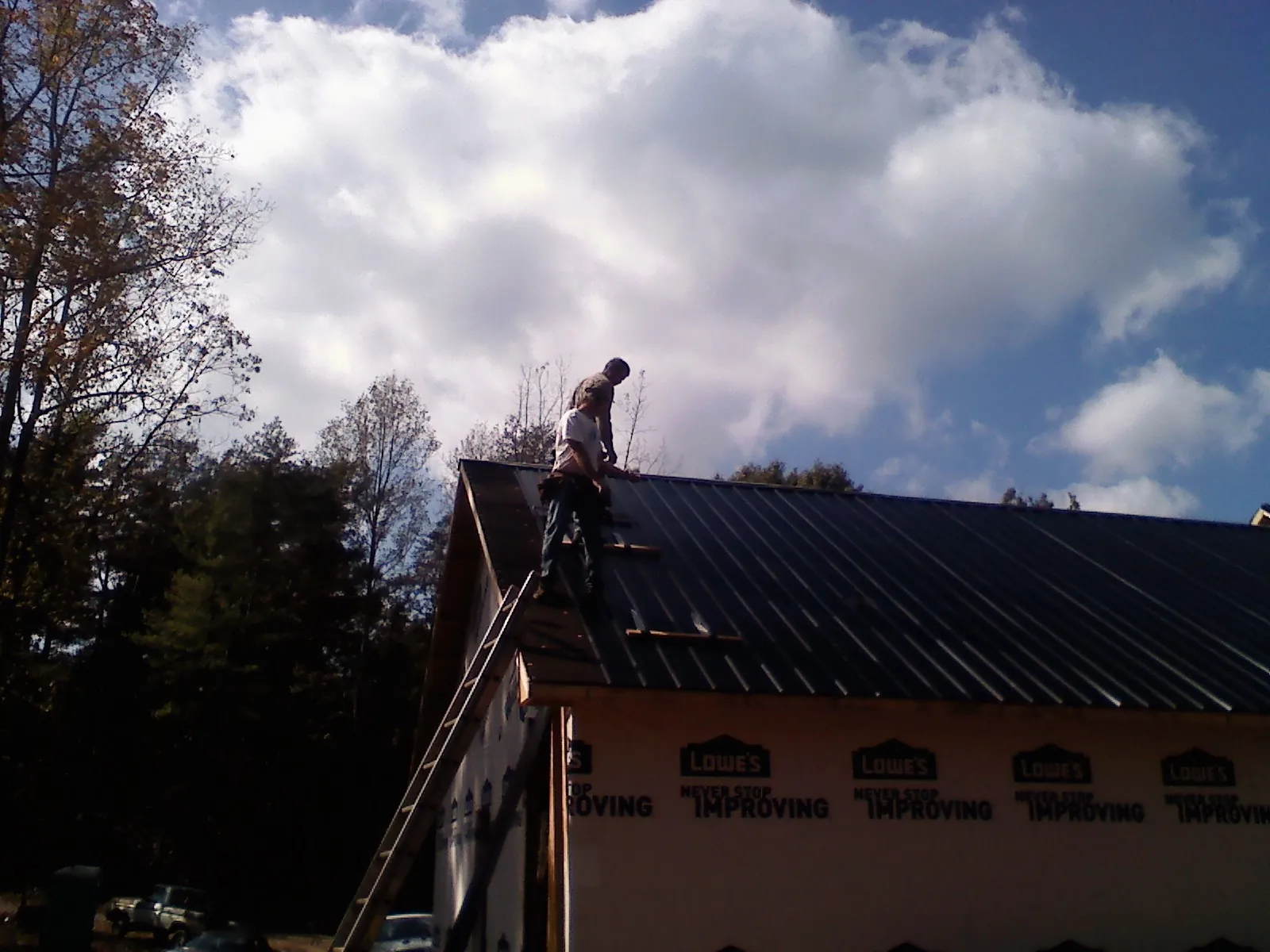 Roofer fastening dark metal panels high against a cloudy sky, from a Roof Inspection job in Elkwood