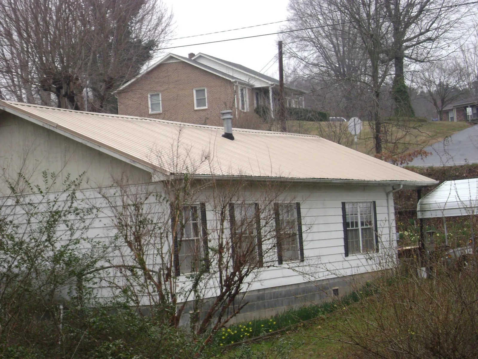 Tan metal roof on a white sided house set into a hillside — Commercial Roofing by Roofing Brothers in Elkwood