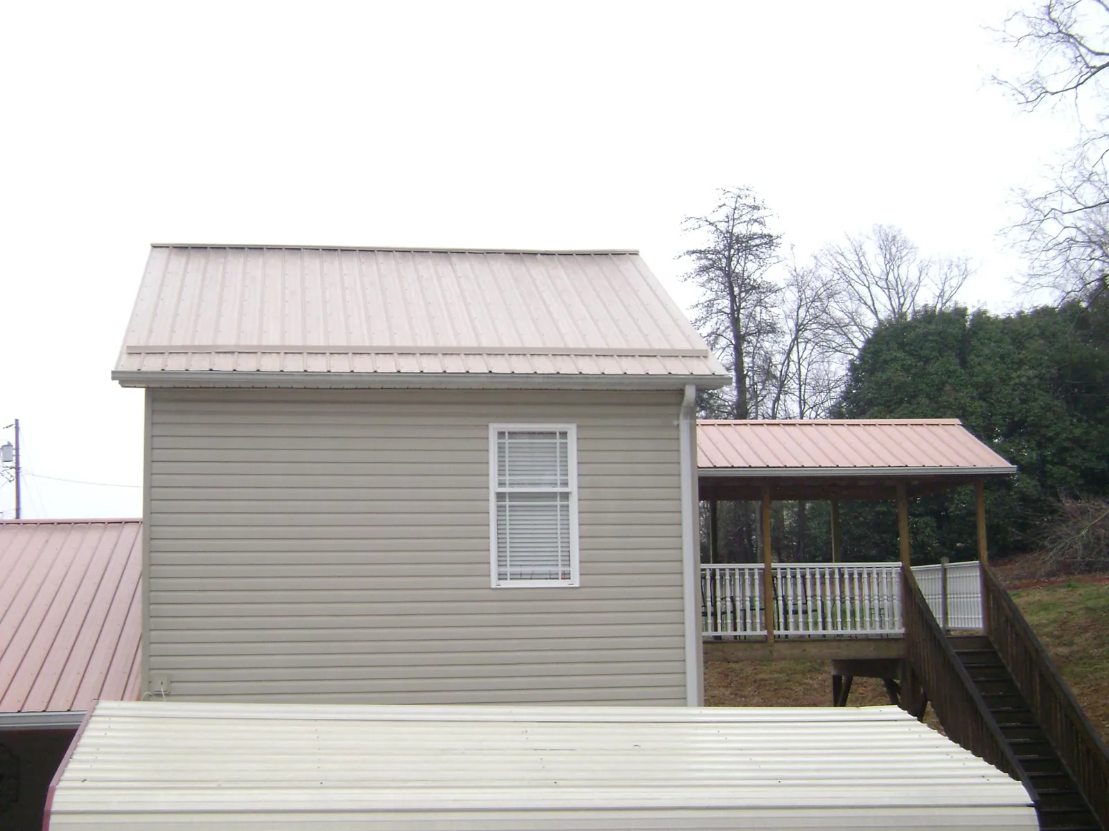 Tan metal roofs on a two story addition and attached porch, from a Roof Replacement job in Elkwood